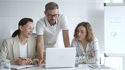 Business team collaborating and analyzing data on a laptop during a dynamic office meeting, uniting efforts to reach shared objectives and drive successful outcomes together