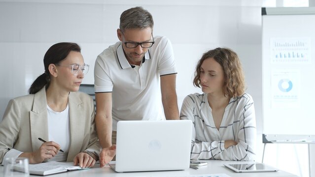 Business team collaborating and analyzing data on a laptop during a dynamic office meeting, uniting efforts to reach shared objectives and drive successful outcomes together