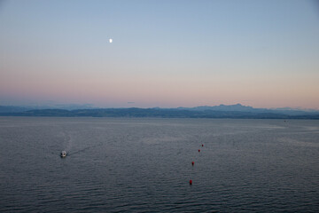 Tranquil evening scene featuring a small boat navigating calm waters under a crescent moon, with distant mountains and a pastel sky creating a serene atmosphere