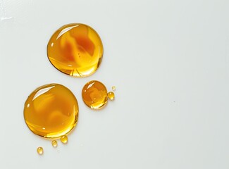 Close-up of three amber liquid droplets on a light surface, with smaller droplets scattered nearby.  The larger drops exhibit subtle internal swirls and reflections