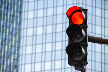 Traffic light displaying red signal against a modern glass building, illustrating urban...