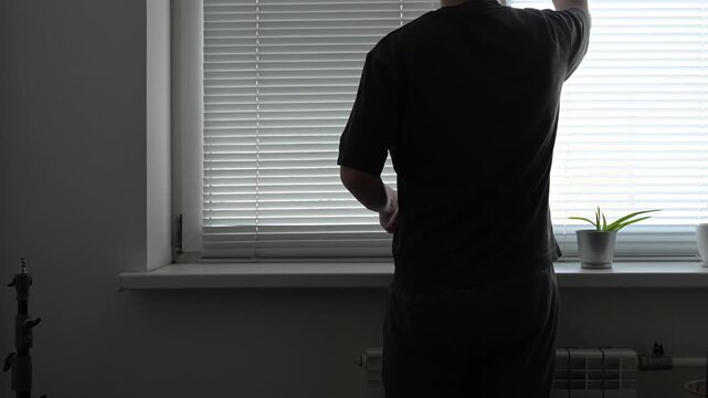 Residential interior showing male hand pulling venetian blinds cord, filling apartment space with natural morning sunlight and creating bright indoor atmosphere