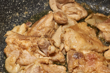 Pieces of chicken meat are fried in a frying pan, exuding flavor and mouth-watering appearance. Delicious chicken pieces are fried in a frying pan until golden brown.