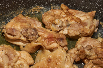 Pieces of chicken meat are fried in a frying pan, exuding flavor and mouth-watering appearance. Delicious chicken pieces are fried in a frying pan until golden brown.