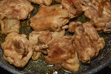 Pieces of chicken meat are fried in a frying pan, exuding flavor and mouth-watering appearance. Delicious chicken pieces are fried in a frying pan until golden brown.