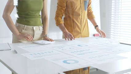 Business professionals reviewing financial charts, calculating data with calculator on table, analyzing statistics during collaborative project meeting.