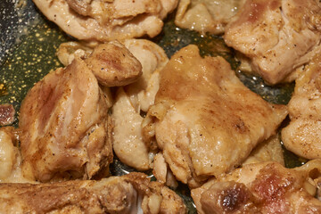 Pieces of chicken meat are fried in a frying pan, exuding flavor and mouth-watering appearance. Delicious chicken pieces are fried in a frying pan until golden brown.