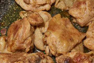 Pieces of chicken meat are fried in a frying pan, exuding flavor and mouth-watering appearance. Delicious chicken pieces are fried in a frying pan until golden brown.