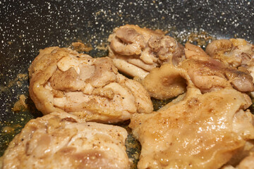Pieces of chicken meat are fried in a frying pan, exuding flavor and mouth-watering appearance. Delicious chicken pieces are fried in a frying pan until golden brown.