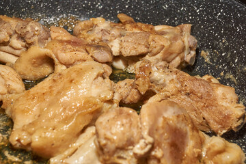 Pieces of chicken meat are fried in a frying pan, exuding flavor and mouth-watering appearance. Delicious chicken pieces are fried in a frying pan until golden brown.