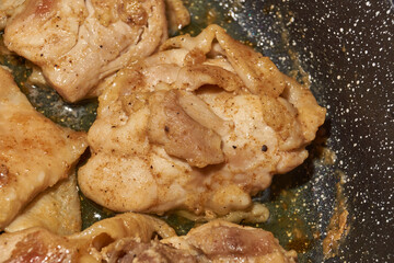 Pieces of chicken meat are fried in a frying pan, exuding flavor and mouth-watering appearance. Delicious chicken pieces are fried in a frying pan until golden brown.