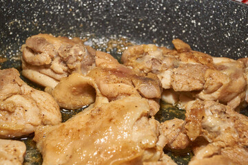 Pieces of chicken meat are fried in a frying pan, exuding flavor and mouth-watering appearance. Delicious chicken pieces are fried in a frying pan until golden brown.