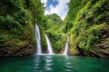 A stunning waterfall flows between dense green vegetation, with clear turquoise water reflecting the surrounding lush landscape, creating a peaceful and inviting scene
