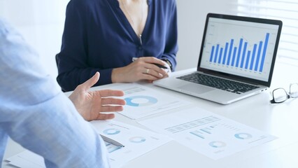 Business professionals collaborating on a laptop, reviewing financial documents, and discussing project strategies in a modern office. Businesspeople in finance concept