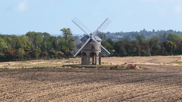 Moving from low to high: A windmill in the English countryside during summer in daylight. Aerial drone footage with superzoom compression in the background. Chesterton mill