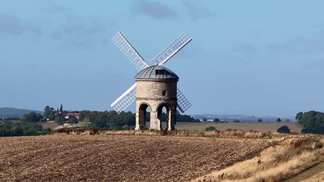Moving from low to high: A windmill in the English countryside during summer in daylight. Aerial drone footage with superzoom compression in the background. Chesterton mill