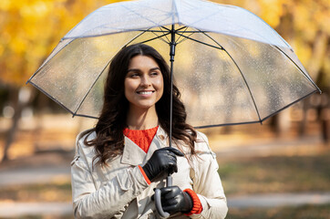 Portrait of cheerful young woman walking under autumn rain at yellow park. Romantic millennial lady enjoying bad weather, spending time outside in rainfall. Colorful season concept