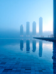 Modern cityscape with high-rise buildings reflected in a calm, blue water pool