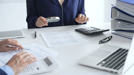 Female financial analysts with male colleague examining documents, using magnifying glass and...
