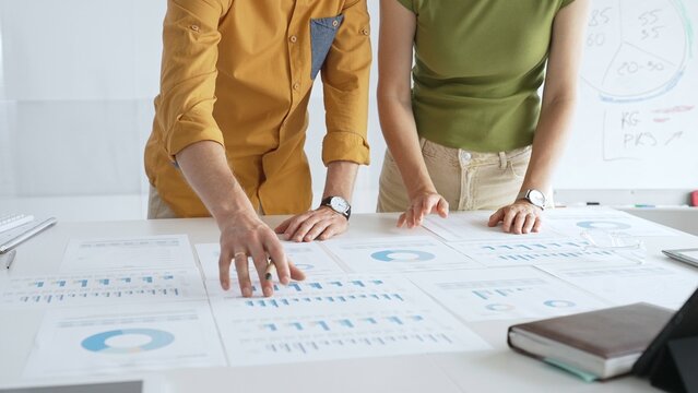 Business professionals analyzing financial reports, pointing at charts during collaborative meeting, discussing data with focused professional demeanor - Powered by Adobe