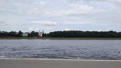Volga River in Tver, Russia, with view of cityscape and green trees along riverbank. Sky is partly cloudy, and water reflects surrounding scenery