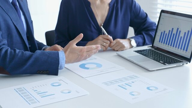Businessman and business woman reviewing financial documents, collaborating over laptop screen, analyzing market charts for strategic corporate planning. Businesspeople and finance concept
