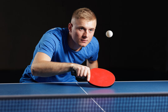 Focused table tennis player serving with red paddle on dark indoor background