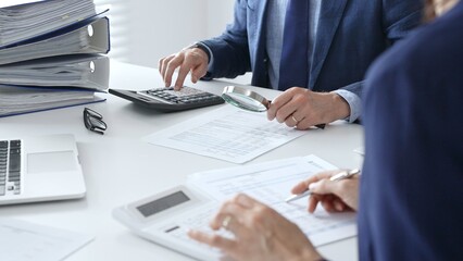 Close up of male financial analysts with female colleague examining documents, using magnifying glass and calculator at workplace in office. Audit and taxes in business