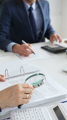Financial analysts examining documents, using magnifying glass and calculator while studying corporate data at workplace. Audit and taxes in business