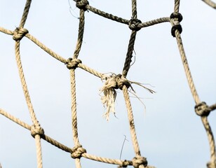 Close-up of a weathered rope net against a pale sky