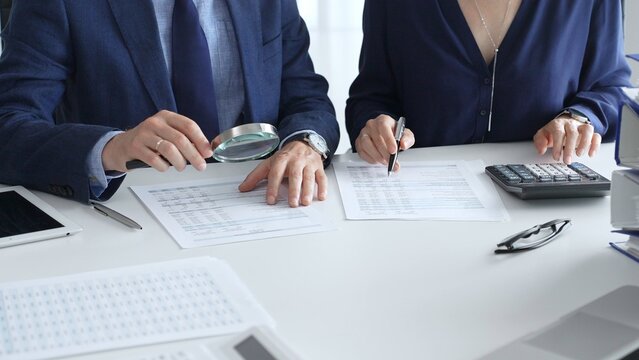 Chartered accountants analyzing financial reports with a magnifying glass and calculator for precise compliance verification. Audit and taxes in business