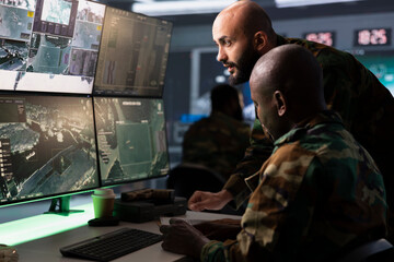 Military team conducts tactical reconnaissance, utilizing devices for data analysis and mission planning. Soldier and colleague use satellite gear to look at aerial map on screen, pinpointing targets