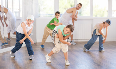 Fototapeta premium Emotional tween girl dancer rehearsing modern krump dance moves during group workout in kids studio under guidance of male instructor