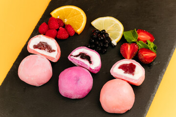 Colorful mochi ice cream with fruity filling on slate board with fresh berries and citrus