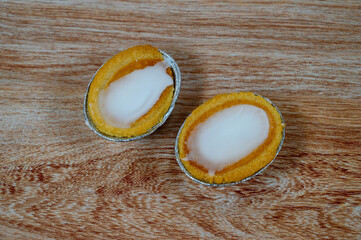 Two oval coconut desserts sit on a textured wooden surface, showcasing a smooth white filling and golden exterior. The treats, flavored with pandan, look appetizing and inviting