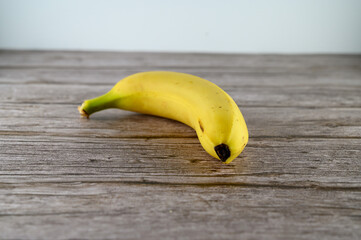 A ripe yellow banana rests on a rustic wooden table, showcasing its smooth skin and natural curves. Ideal for snacking or adding to dishes