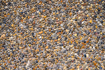 A vibrant collection of smooth pebbles and stones covers the ground, revealing a rich array of colors and textures. Sunlight highlights the natural beauty of this gravel surface