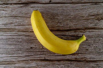 A ripe yellow banana rests on a rustic wooden table, showcasing its smooth skin and natural curves. Ideal for snacking or adding to dishes