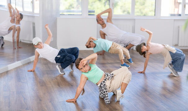 Preteen girl performing hip hop dance moves, showcasing skills and concentration, during group class for kids led by young male instructor in street dance studio.. - Powered by Adobe