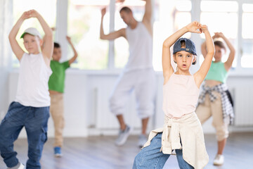 Naklejka premium Focused preteen girl performing dynamic hip hop moves in group class for kids, led by skilled young male dance instructor in vibrant urban studio