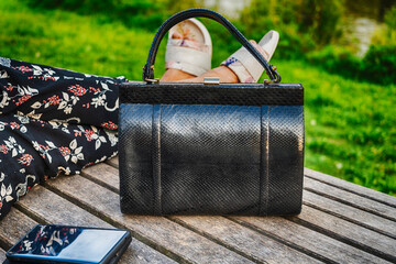 Women's snake leather bag and phone at feet