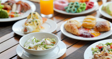 Assorted breakfast buffet on wooden table, featuring eggs benedict, pastries, juice. Vibrant, colorful brunch setting, variety, freshness, hospitality, dining experience.