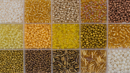 Close up of colorful yellow and gold seed beads in square sections flat lay background