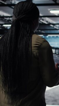 Vertical video Engineer in data center using tablet to deploy secure server architecture. African american woman in server hub using device to do rollout of cybersecurity framework, camera A