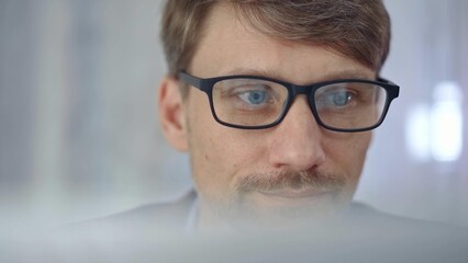 Businessman with glasses looking intently obscured partially by a translucent surface of laptop....
