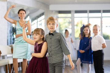Obraz premium Smiling junior schoolchildren in party dresses learning dancing waltz with pedagogue in social hall