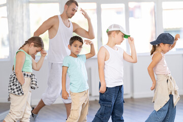 Fototapeta premium In sports studio, creative childrens team learns hip-hop dance accompanied by experienced man teacher