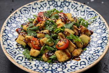 Crispy eggplant salad with cherry tomatoes, herbs and sesame sauce in patterned bowl