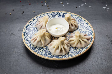 Traditional Georgian khinkali dumplings with sour cream sauce on ceramic plate