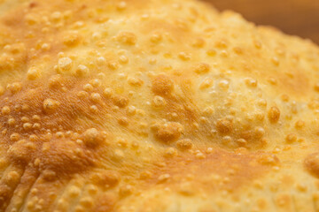 Traditional deep fried cheburek with golden crust served on wooden board, top view